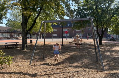 The schoolyard with a swing and seating area under the trees.
