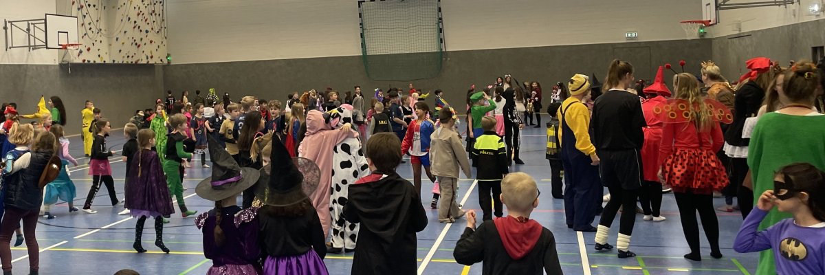 Karnevāla ballīte sporta zālē ar daudz bērniem krāsainos tērpos.