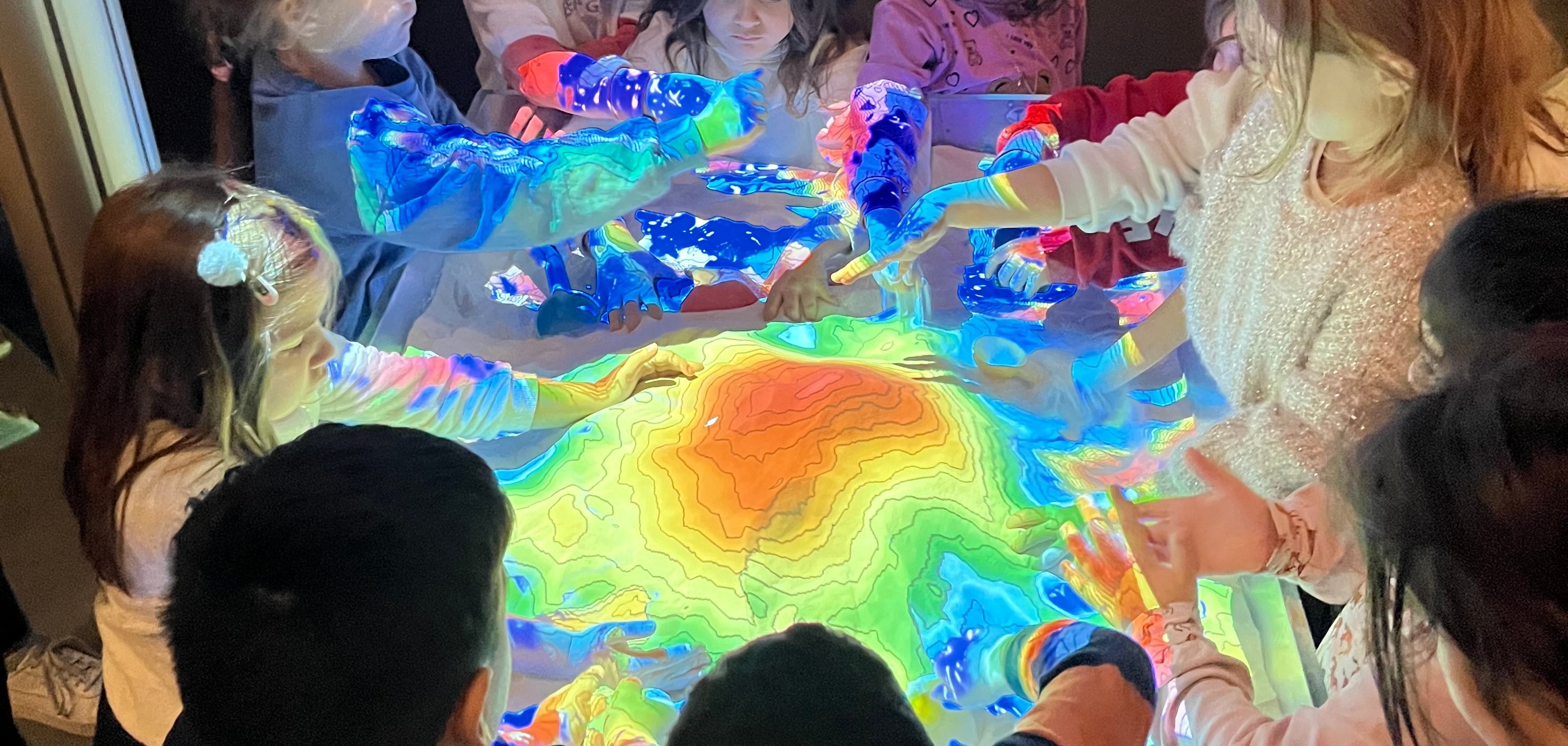 Noen barn står rundt "Reality Agumented Sandbox", som representerer de geofysiske sammenhengene i en modell.