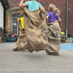 Sportfest - Kinder treten im Sackhüpfen gegeneinander an.